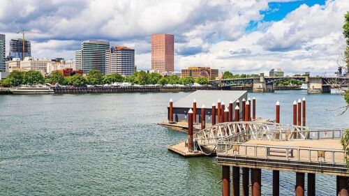A ramp leads down to a river dock with skyscrapers on the other side of the water