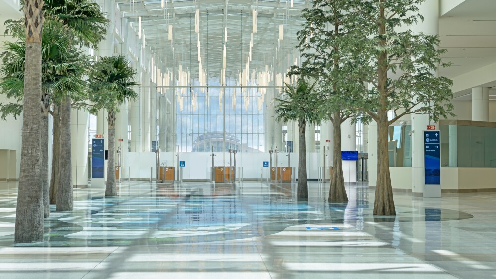 An open arrivals corridor with indoor trees, high ceilings, and dangling lights.