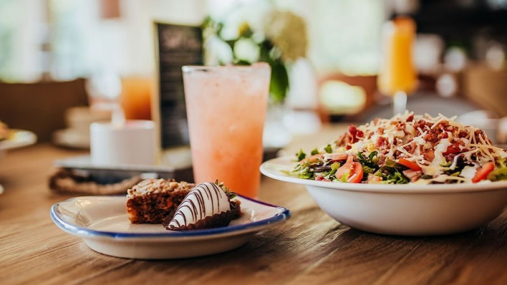 A pink-colored drink, salad, and two desserts including a chocolate covered strawberry sit on a table.