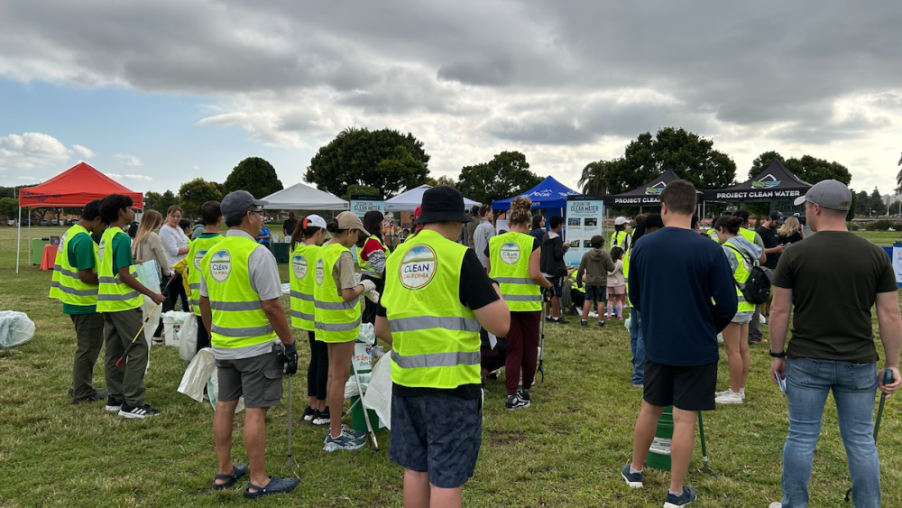 A group of volunteers wearing bright yellow vests and holding trash-picking tools get ready to help with a litter cleanup event.