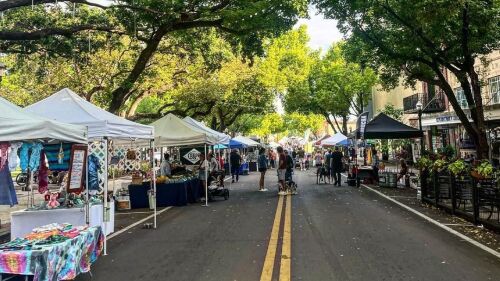 A downtown Lakeland street lined with tents selling farmers market goods. Trees hang over the street.