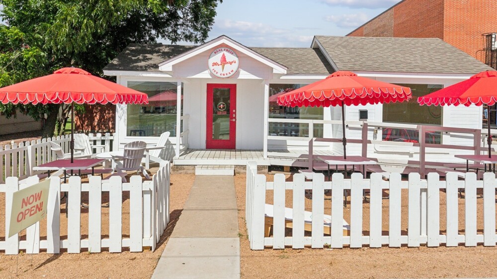 Photo of a white house with red umbrellas in the yard that has been converted into an ice cream shop. 