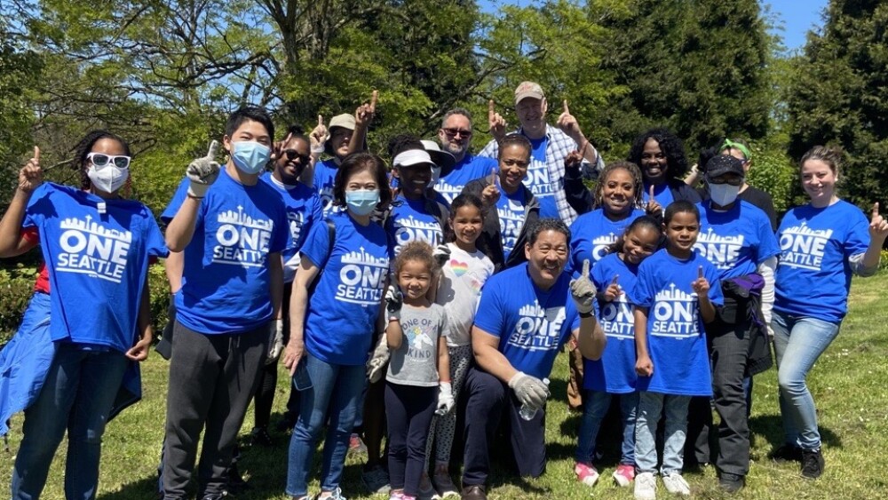 Seattle Mayor Bruce Harrell poses with kids and other volunteers wearing blue One Seattle t-shirts in a field.