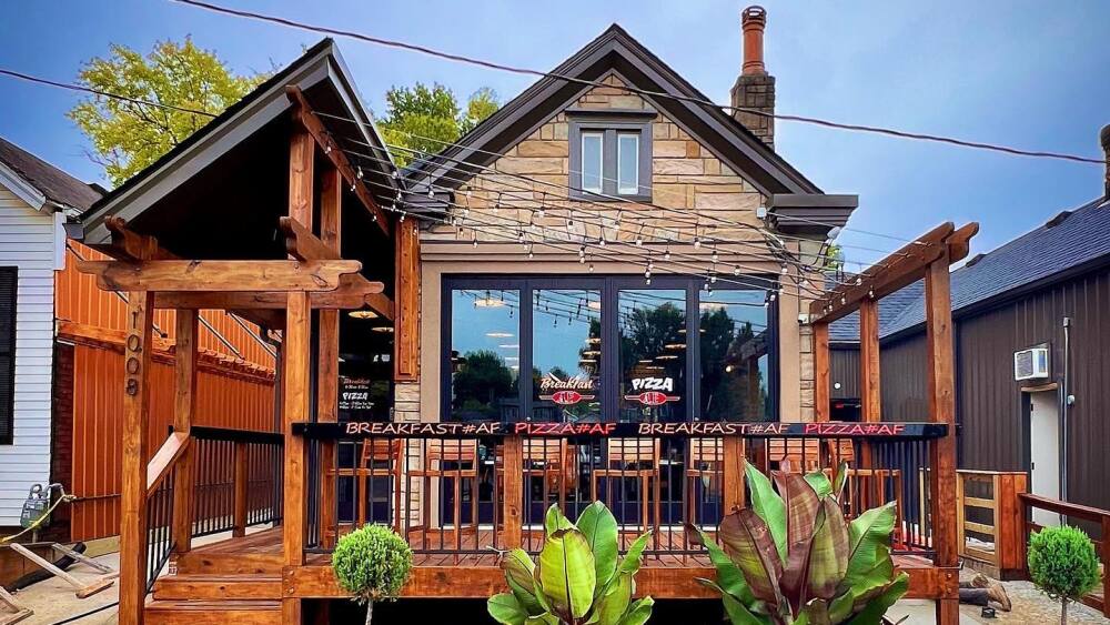 A triangular, stone covered building, with wooden front porch, stained deep red.