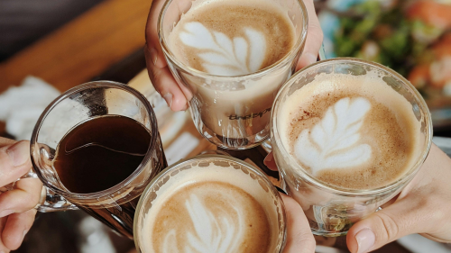 Four people share a toast while holding coffee and lattes ranging in color from deep brown to light brown.
