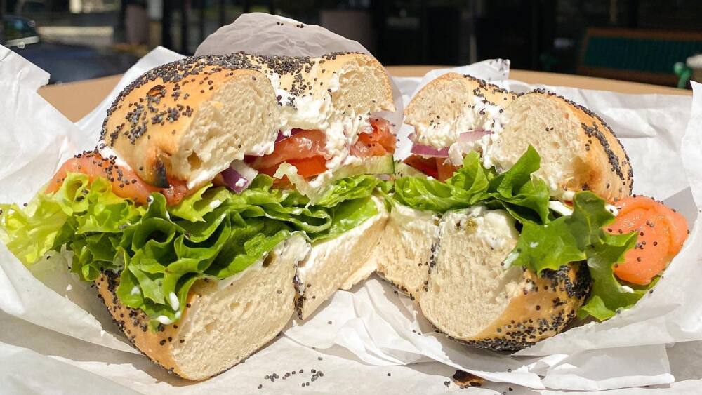 A cross-section of a bagel sandwich with lettuce + tomato in front of Saratoga Bagels. 