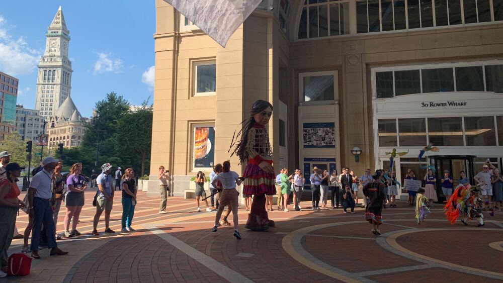 Little Amal walks through a crowd gathered at Rowes Wharf