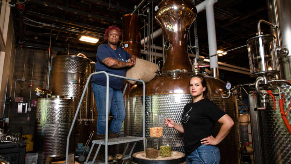 Two female distillers pose in front of a large still at Freeland Spirits