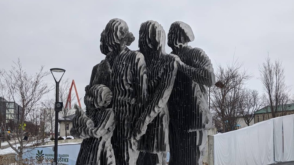 A metal statue depicts five individuals on a round platform surrounded by snow.