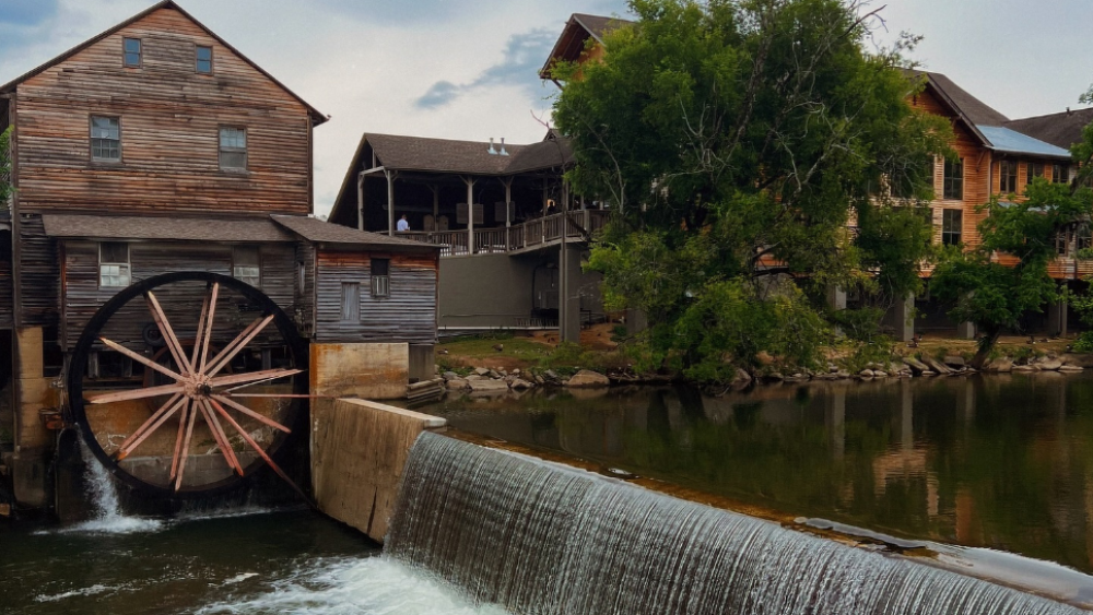 A multi-building wooden structure with a waterfall and wooden wheel attached to the side of the building.