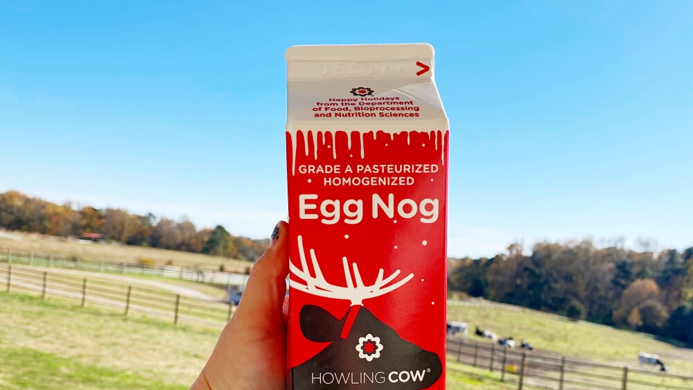 Someone holding up a Howling Cow Egg Nog in front of a pasture.