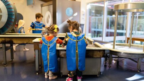 Kids standing in front of a table at the Thinkery.