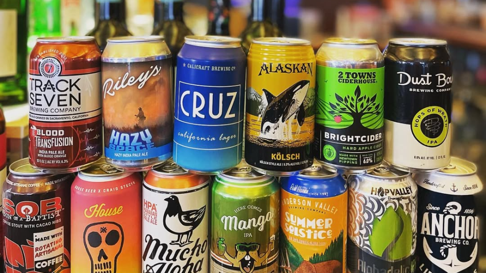 A group of 13 colorful craft beer cans stacked in two rows with a bar in the background.