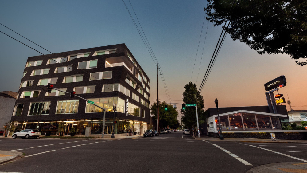Jupiter Hotel sits on the right, with the 6-story Jupiter NEXT on the left. Both sit along East Burnside Street and are lit by a late sunset.