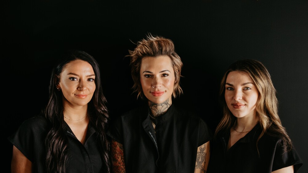 three women wearing black stand in front of a black background