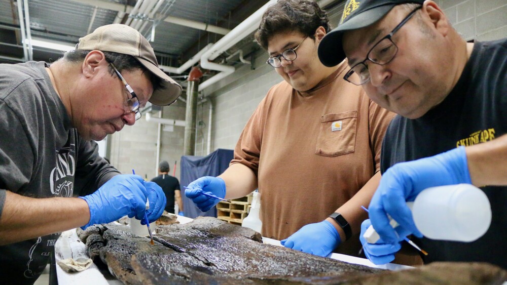 Three men examine an ancient dugout canoe in a lab.jpeg