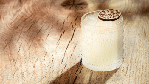 A very light yellow drink sits in a short glass garnished with freeze-dried fruit.