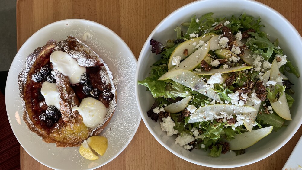 Two plates of food, one that has a Dutch Baby Pancake and the other with a chopped salad. 