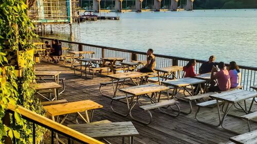 People sitting at picnic tables on the dock outside Mozart's Coffee Roasters, with Lake Austin in the background.