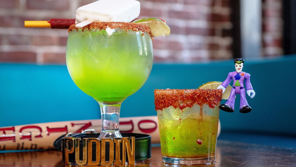 Two bright green cocktails with Tajin rims; a tiny Joker figuring hangs from one of the glasses.