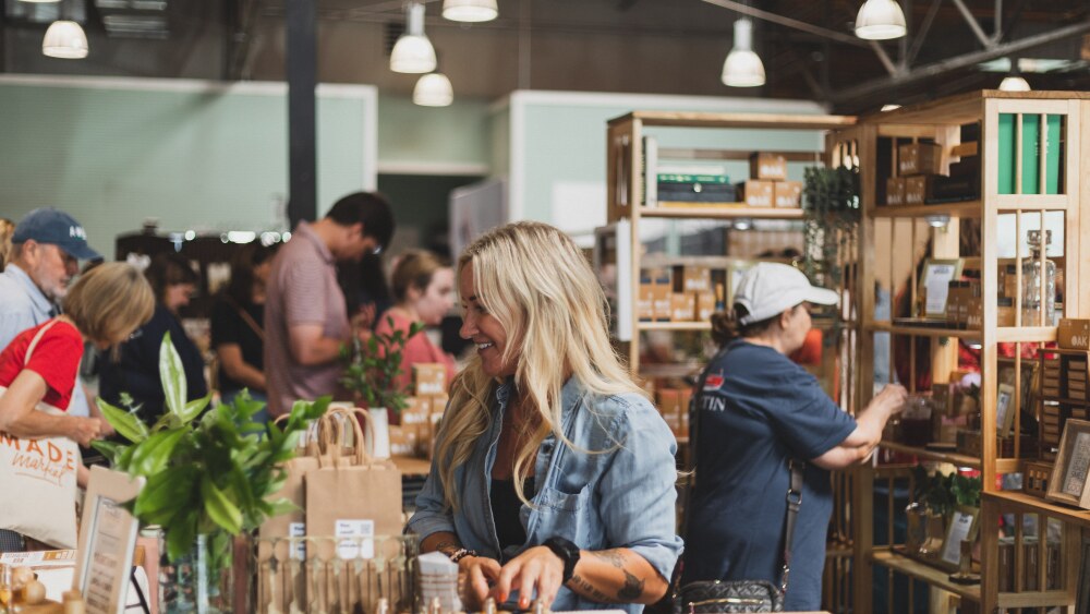 a girl stands behind a table with glassware and bags on top of it