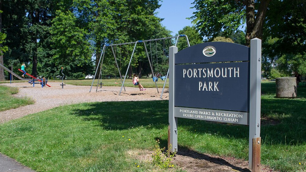A sign reads Portsmouth Park and there are kids swinging and playing on a seesaw in the background.