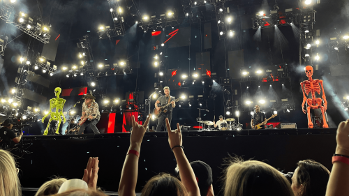 A fan holds up the rock on sign while Brothers Osborne performs on the Nissan Stadium stage with two larger than life skeletons.