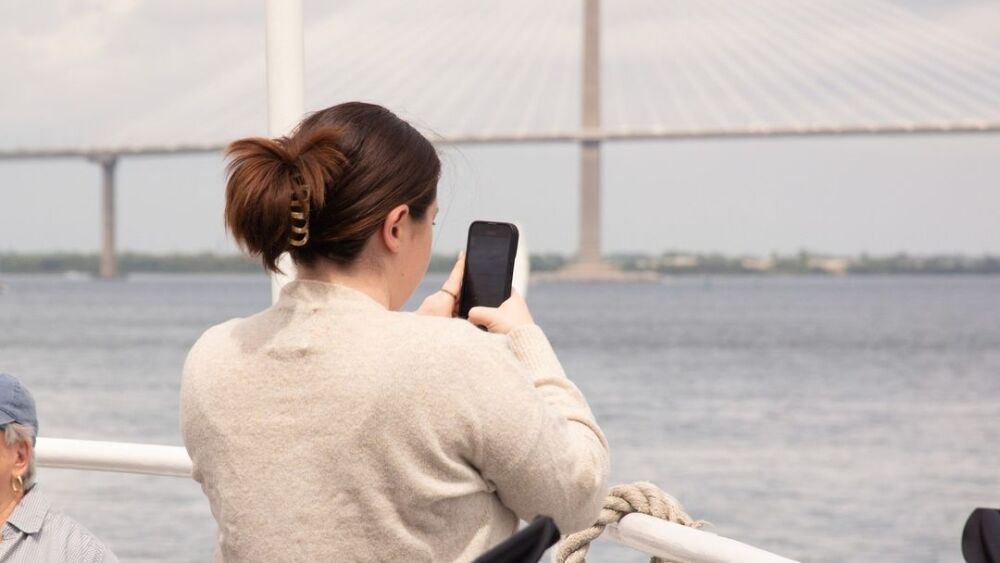 person with cream colored sweater on boat taking a picture of the water with cell phone