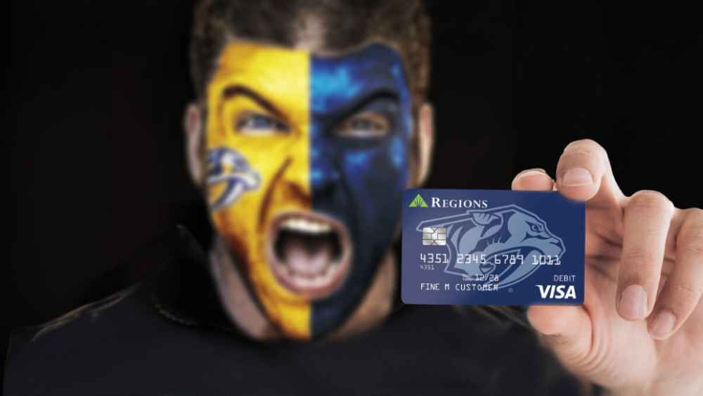 A person wearing yellow and blue face paint holding up a custom debit card against a black background