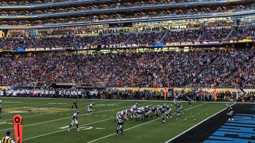 A stadium packed with thousand of people watch NFL players on the football field during the Super Bowl.