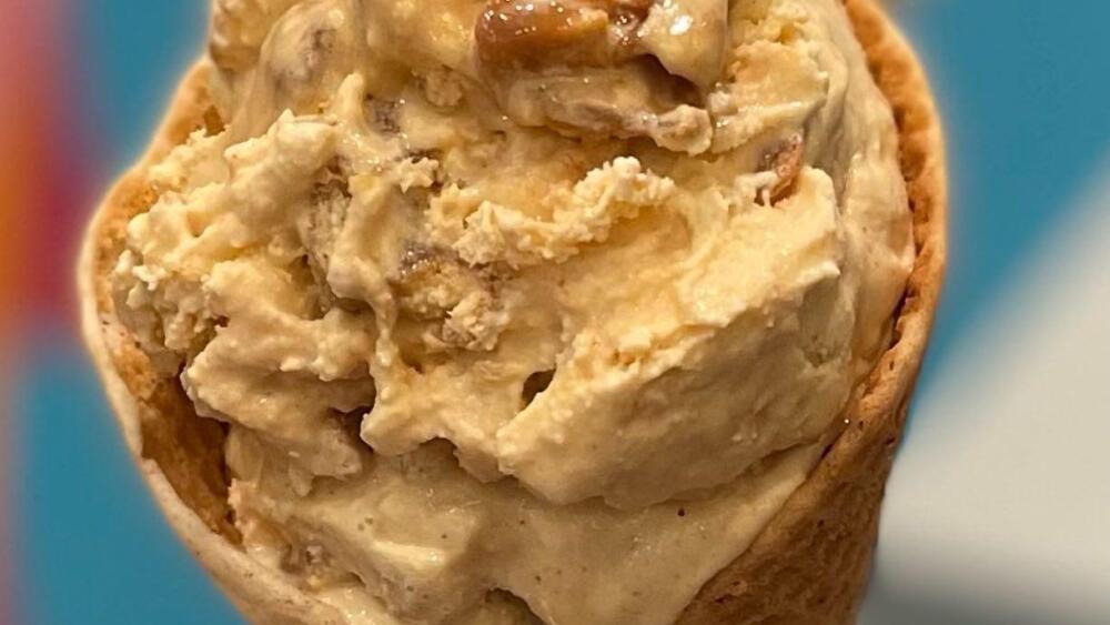 A thick scoop of ice cream in a cone shows bits of chicken + waffles.