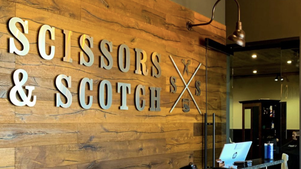 Pictured is the Scissors & Scotch front desk with a wood panel background and a black desk