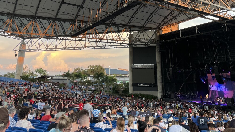 An ampitheatre with the sun setting in the background and a large crowd.
