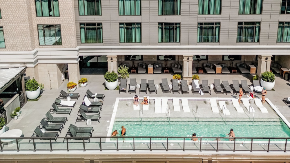 A view of the pool at the Thompson Savannah hotel; there are white lounge chairs in the water and other lounge chairs across the pool area, and several people in and around the pool.
