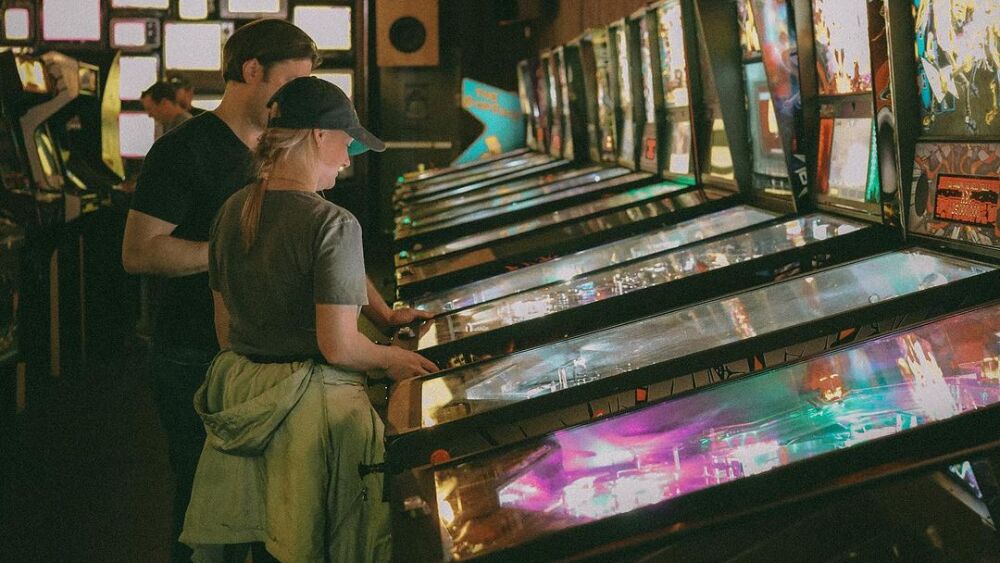 A man and woman standing in front of a row of pinball machines