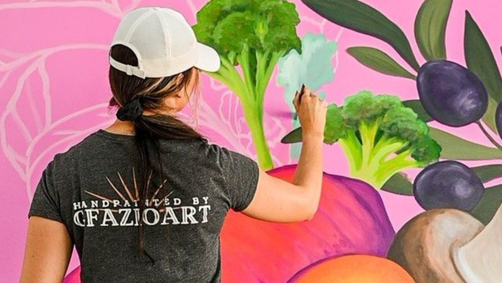 Artist Gillian Fazio painting a colorful mural at Fresh Kitchen