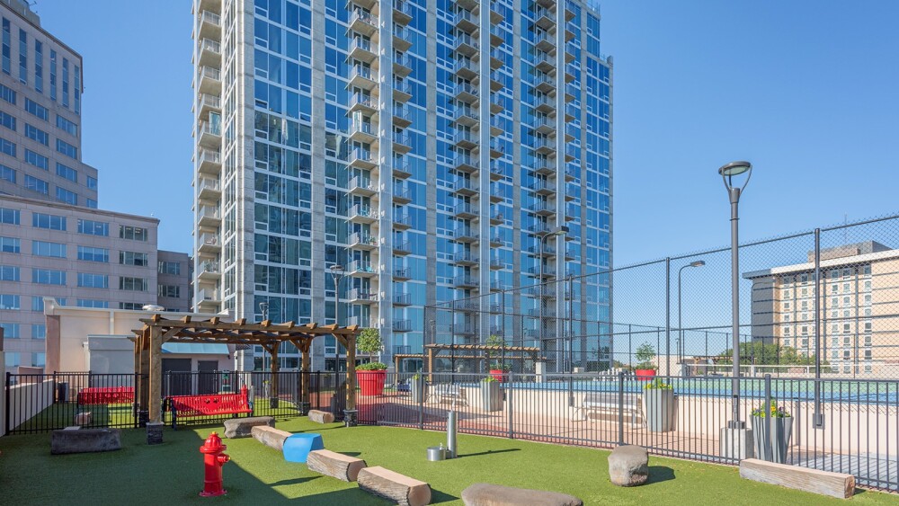 An outdoor view of an apartment building overlooking a rooftop urban park and tennis courts.