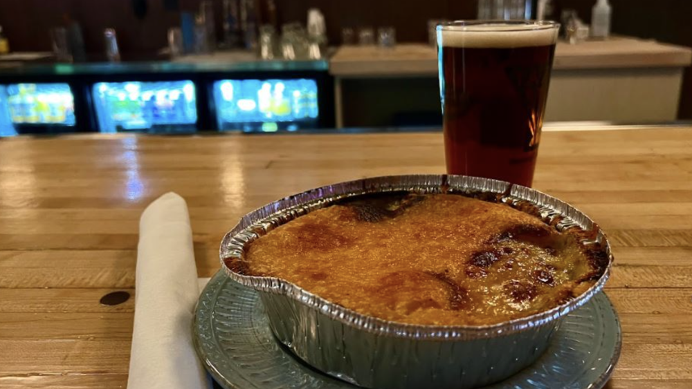 A plated shepherds pie and glass of frothy beer placed on a counter.