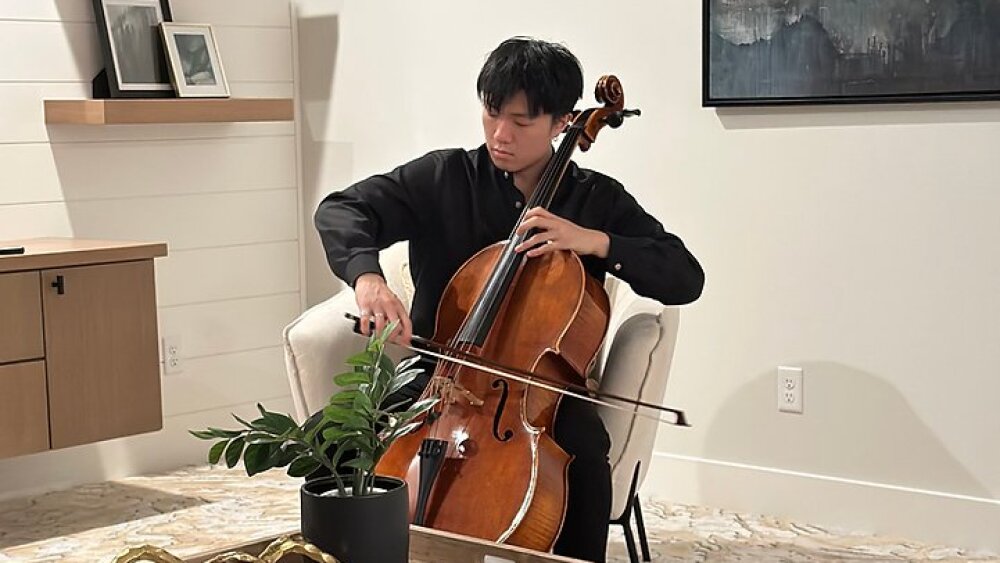 A cellist sits in a light living room playing his instrument