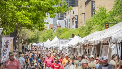 Crowds walk through Main Street in downtown Fort Worth during the Main St. Arts Festival; white tents filled with artists and vendors line the path.
