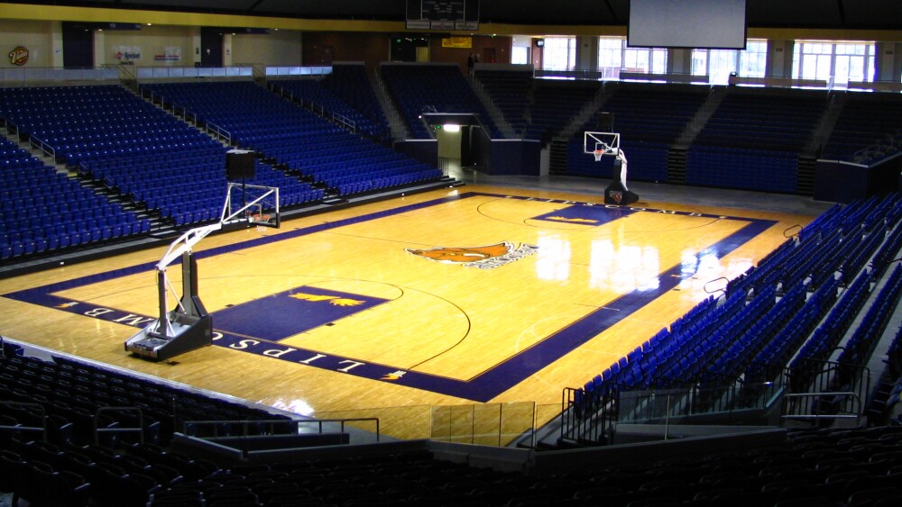 An empty Allen Arena with a projector screen halfway pulled down on the opposite end of the court above the goal and the photo snapped from the corner of one of the sets of bleachers.