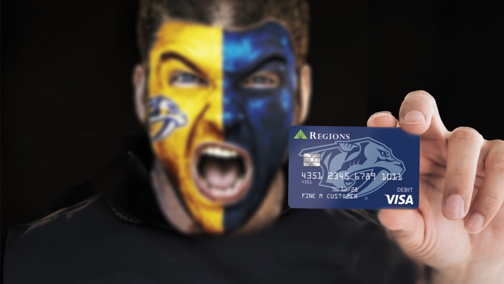 A man with yellow and blue face paint on holding up a Nashville Predators Visa Debit Card while cheering.