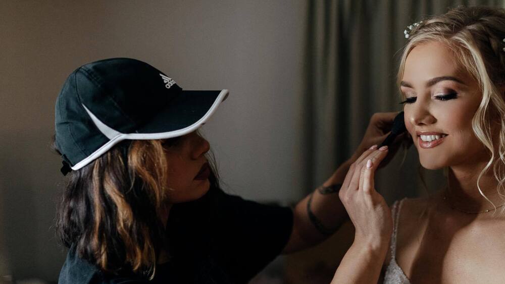 A woman puts makeup on a bride