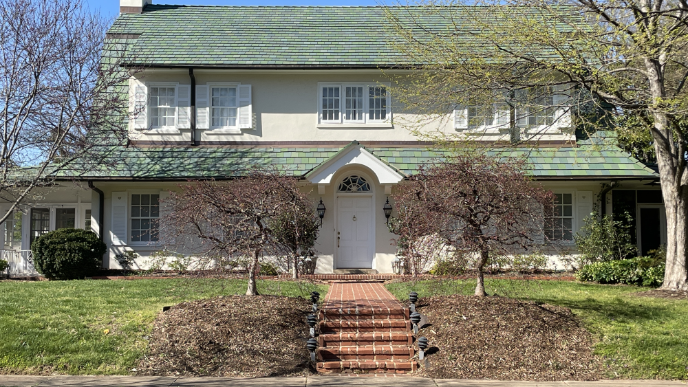 Cream house with green tiled house. A tree is on either side of the brick walkway.