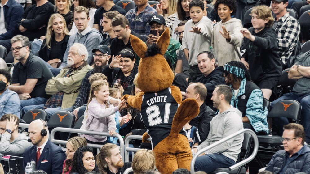 The Spurs Coyote leans over to shake hands with a little girl in the crowd.