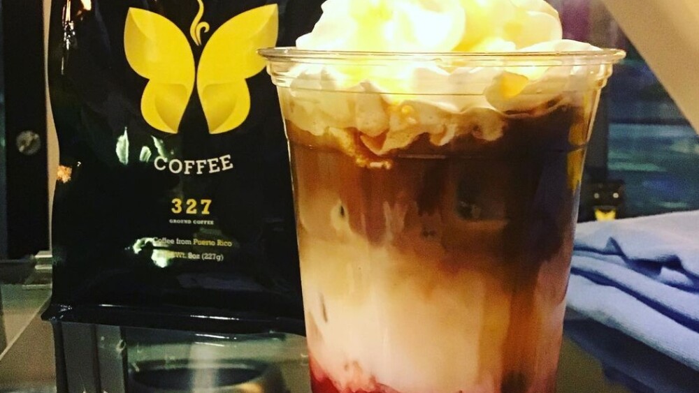 A black bag of coffee beans with the Yellow Butterfly label next to a frothy raspberry smoothie-like drink.