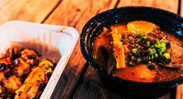 Meat on skewers next to a bowl of ramen in a rich brown broth.