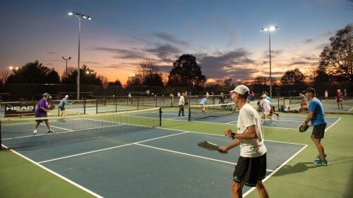 A group of men playing pickleball under lighted courts.