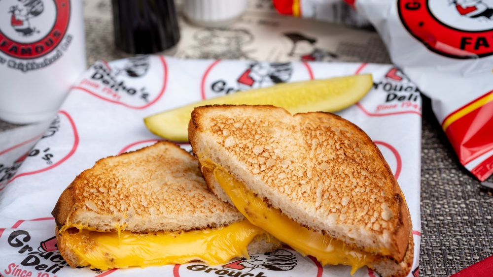 A closeup of a grilled cheese sandwich from Groucho's Deli in Columbia; the yellow cheese is melted between golden brown bread and there's a pickle spear on the side.