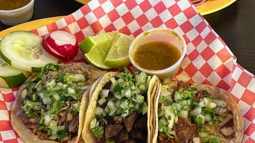 Two baskets of tacos with green salsa and lime on the side